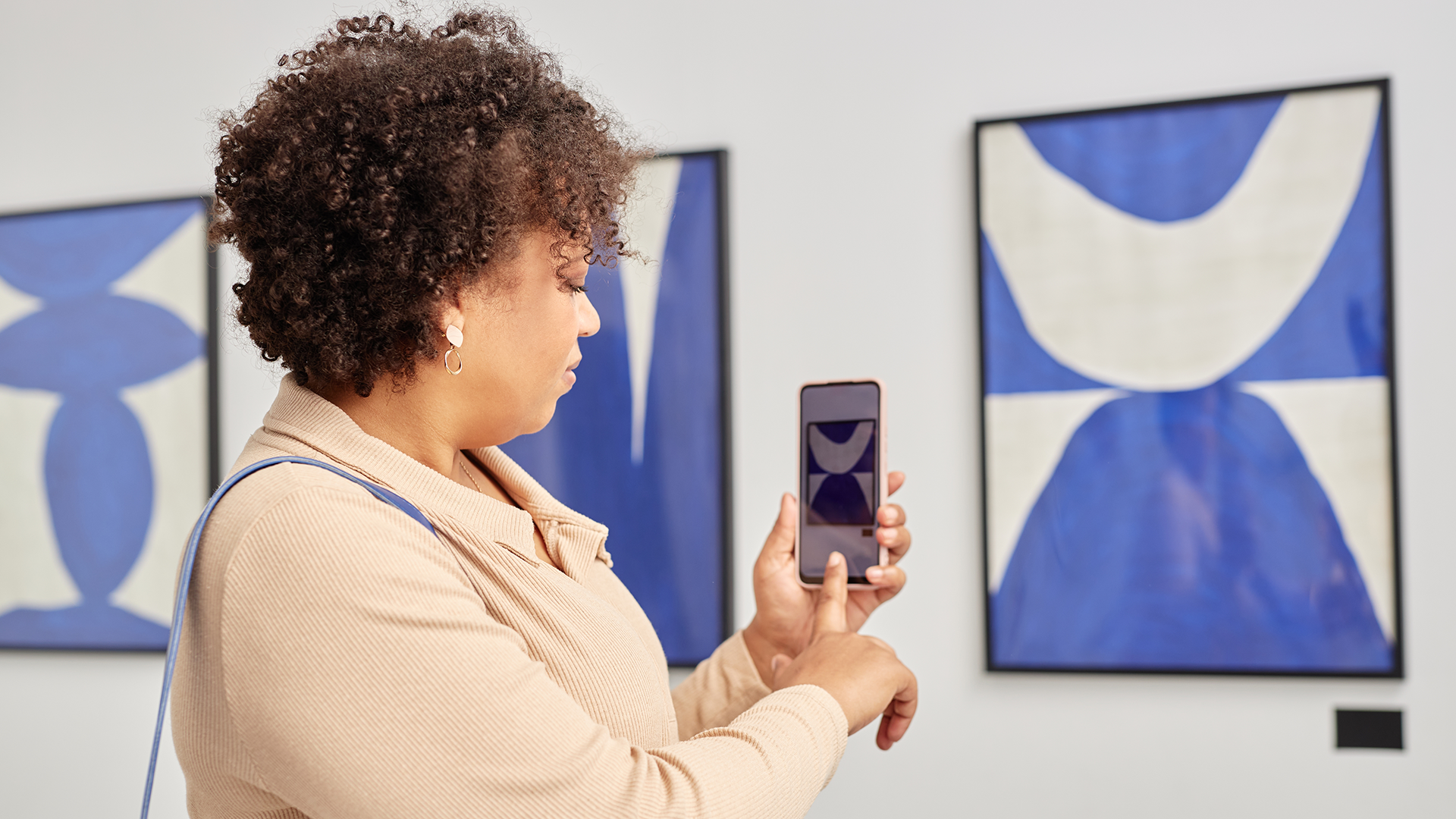A color photo of a woman using her phone to view art at a museum. Shutterstock