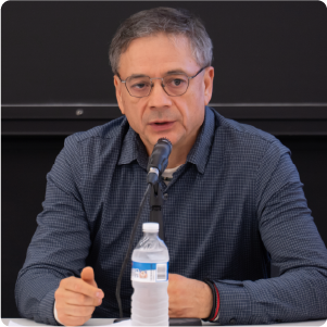 A color photo of a man speaking behind a microphone.