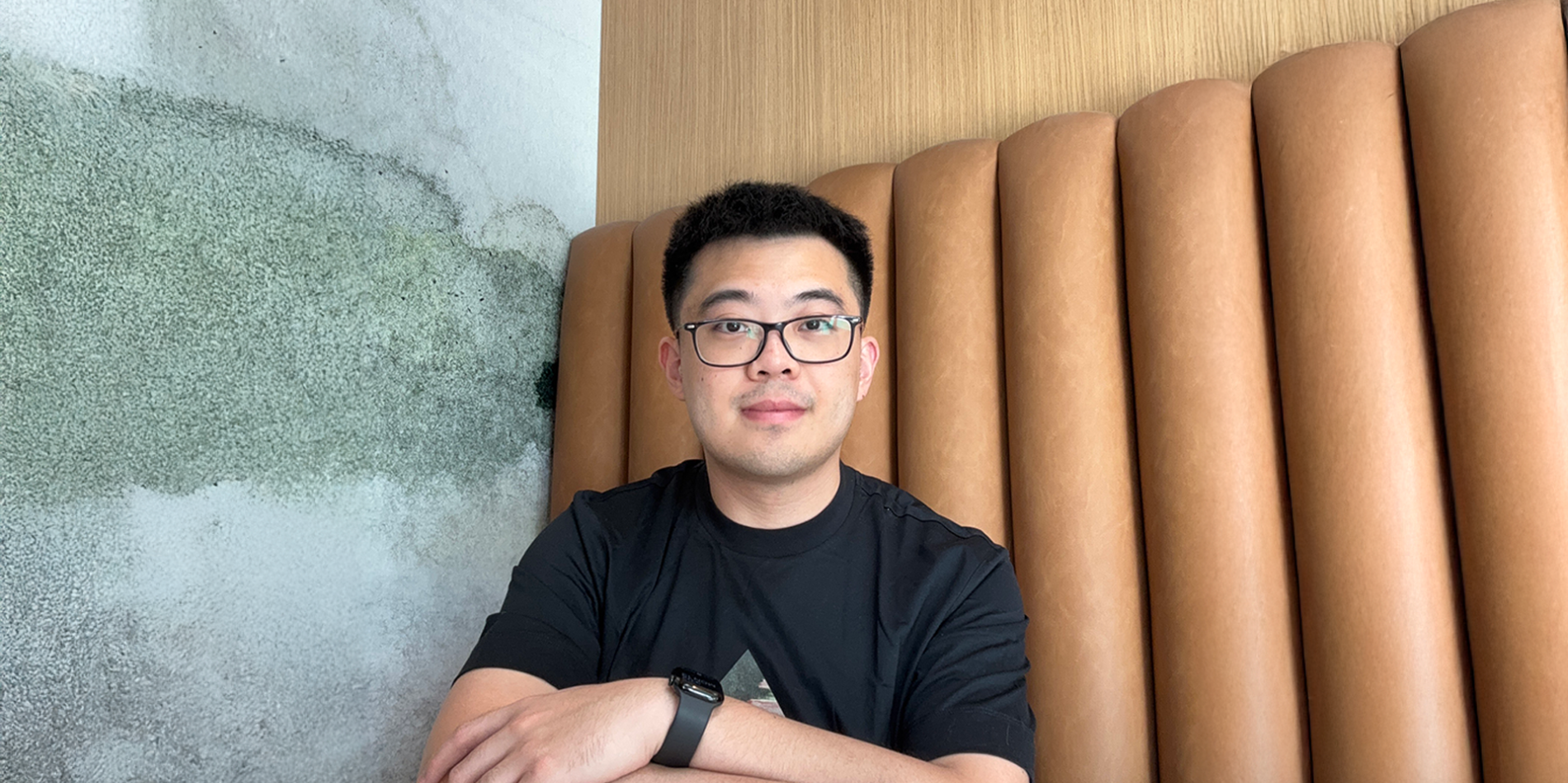A color photo of a man with glasses sitting in a restaurant booth.