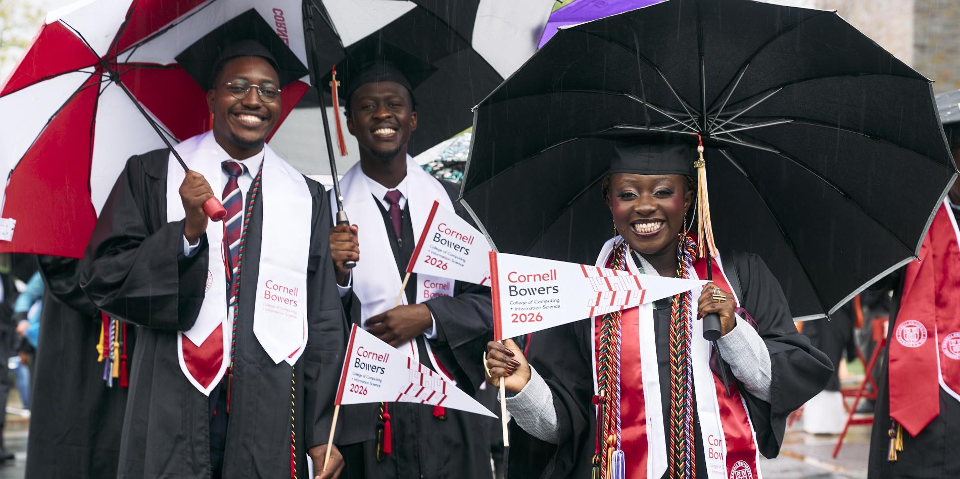 a group of graduates smile under their umbrellas during the procession