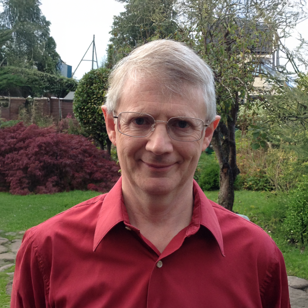 A color photo of a man with glasses standing outside.