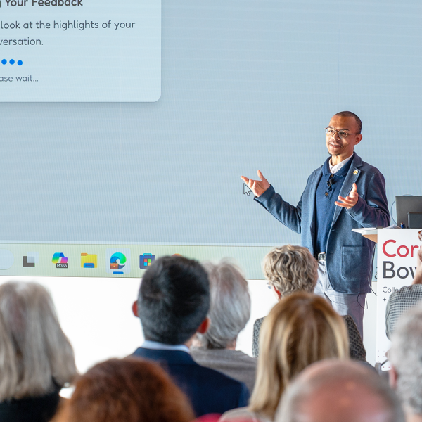 A color photo of a man giving a presentation in front of a large screen.