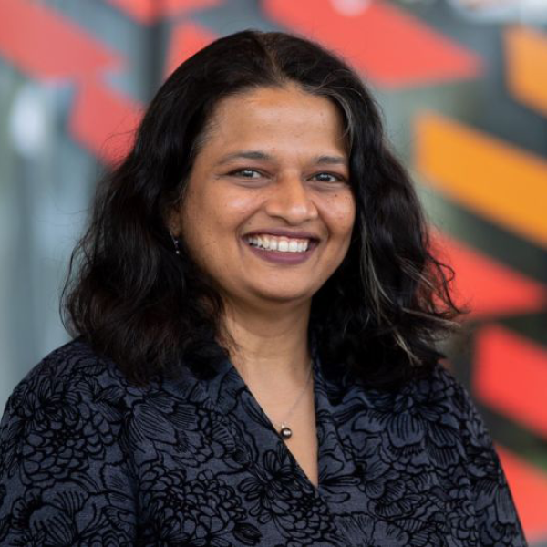 dark haired woman with dark hair smiles in front of a building with red and orange streaks