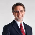 A photo of Haym Hirsh, a smiling man with brown hair and glasses in a navy suit and red tie, in front of a gray background