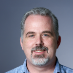 Aphoto of Walker White, a smiling man with short gray hair, a mustache, goatee and a blue check shirt. 