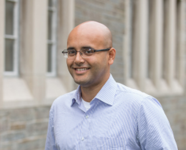 A color photo of bald man with glasses smiling at camera