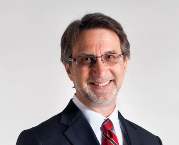 A photo of Haym Hirsh, a smiling man with brown hair and glasses in a navy suit and red tie, in front of a gray background