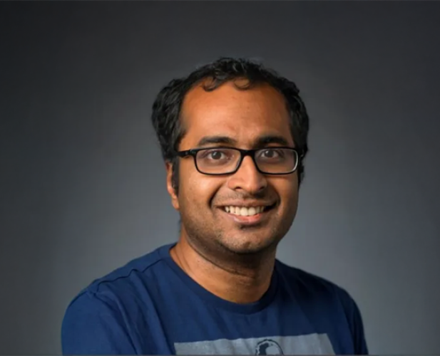 A photo of Bharath Hariharan, a smiling man with short dark hair, glasses and a blue shirt in front of a gray background