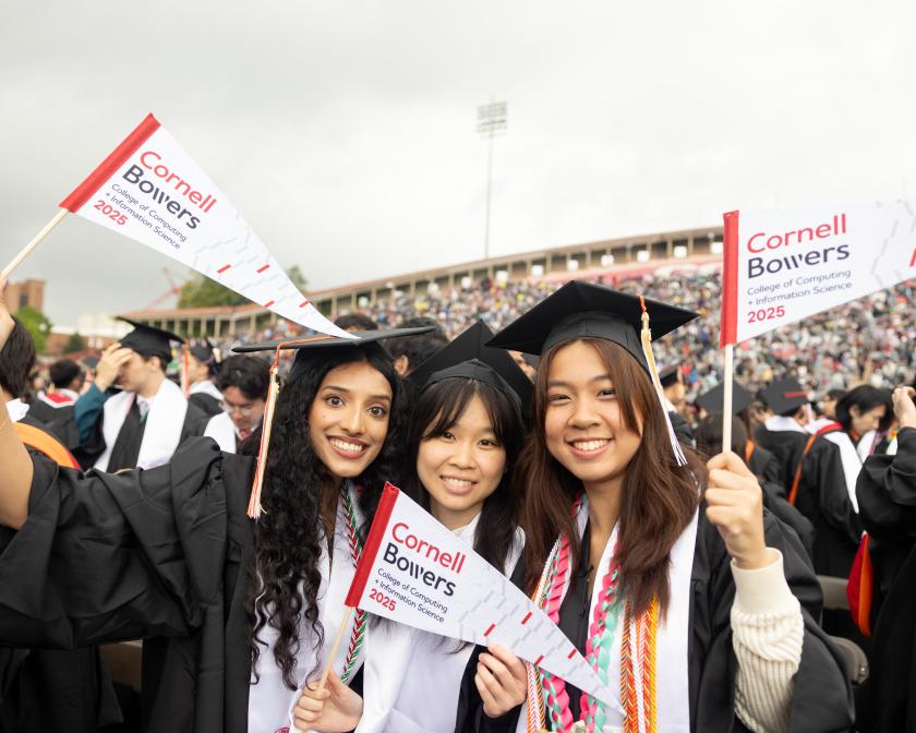 three female graduates wearing black caps and gowns wave white flags