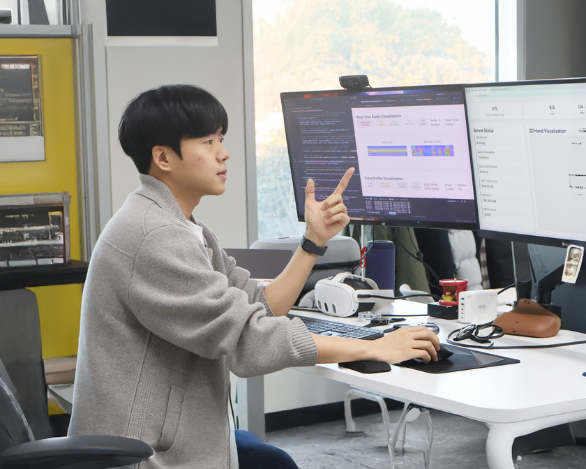 A color photo of a man working at 2 computer screens.