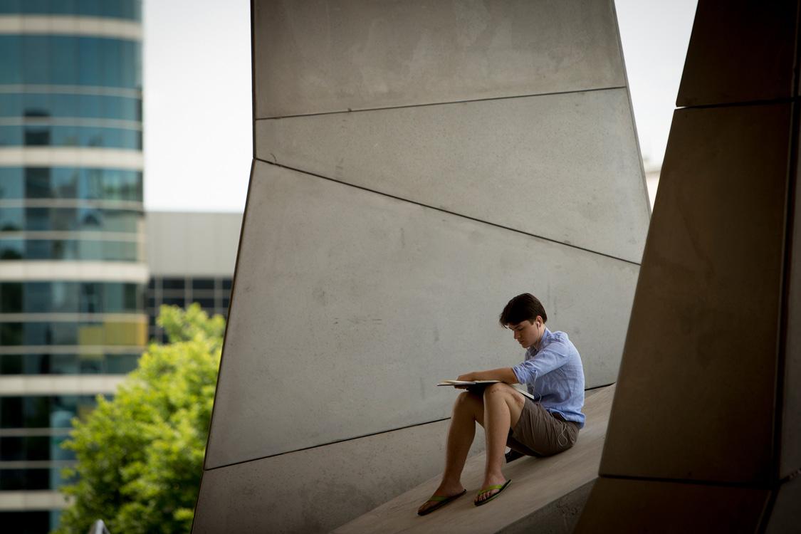 a male student sits outside on the concrete ledge outside Gates Hall in summer